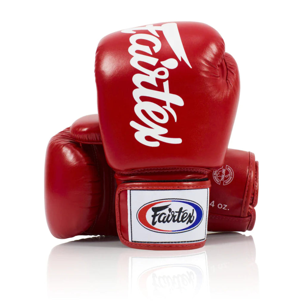 A pair of red Fairtex boxing gloves with the brand logo in white on the cuffs, designed for tight-fitting and compact use.