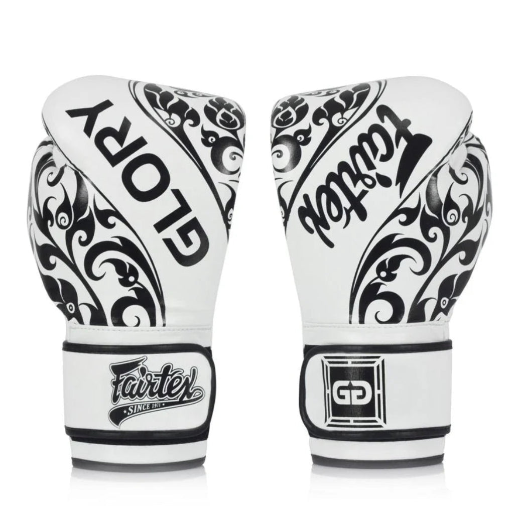 A pair of white and black Fairtex Glory boxing gloves shown from the back, featuring ornate black scrollwork patterns and the brand name 'GLORY' on the back, set against a plain white background.