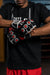A close-up of a person wearing black fingerless MMA sparring gloves with red and white circular grip details, paired with a black t-shirt and red shorts.
